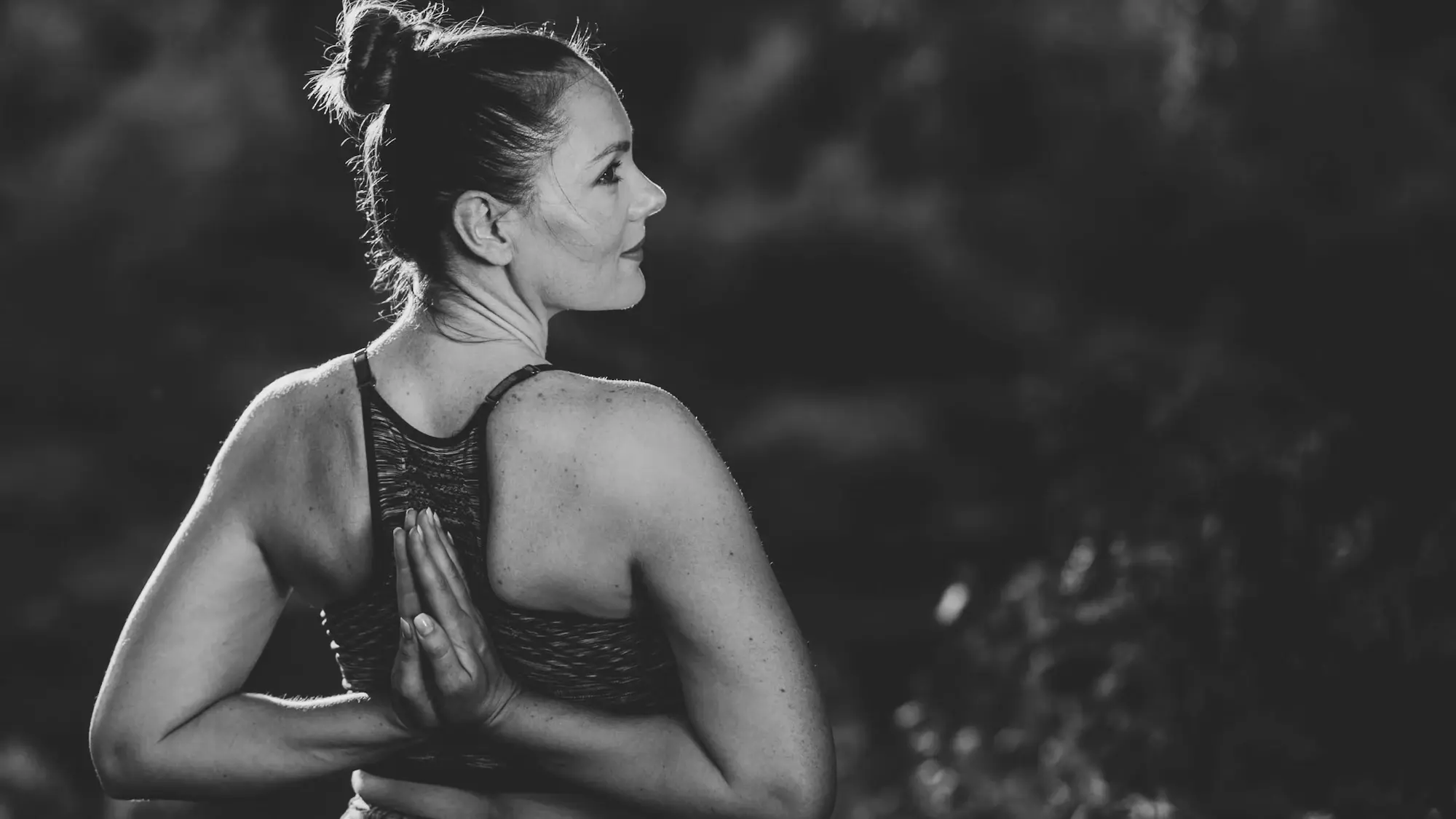 Zajęcia Joga kręgosłupa i bioder w Teho Sport w Trzebownisku — kobieta w pozycji stojącej z dłońmi złożonymi za plecami, zdjęcie czarno-białe