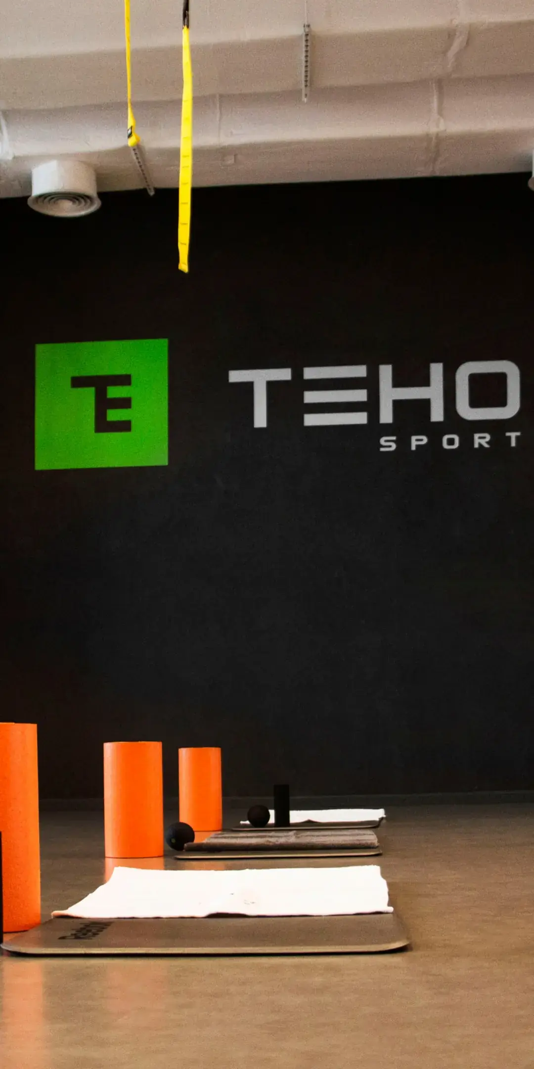 Sala zajęć fitness Teho Sport — maty i wałki do rolowania pod logo na ścianie
